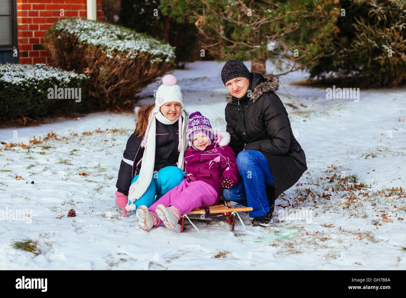 Junge Mutter und ihre Töchter, die Spaß am Wintertag kleine Mädchen spielen auf der Straße im Winter Stockfoto