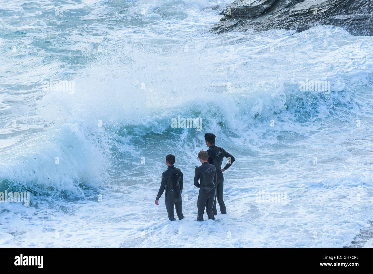 Drei Jugendliche stehen am Strand von Little Fistral wie raue Wellen an Land abstürzen. Stockfoto