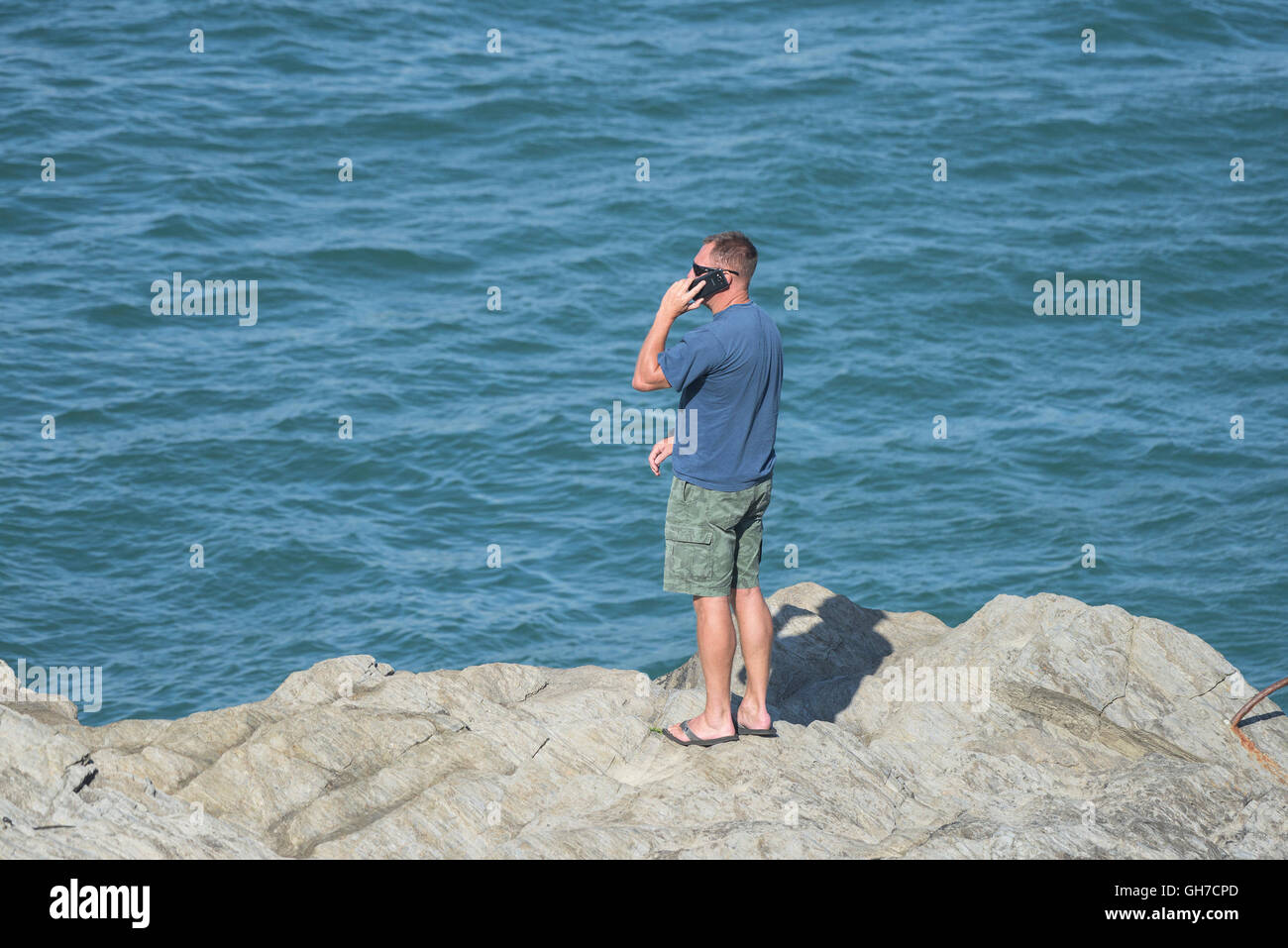 Ein Urlauber nutzt ein Handy, steht er auf Felsen am Meer. Stockfoto