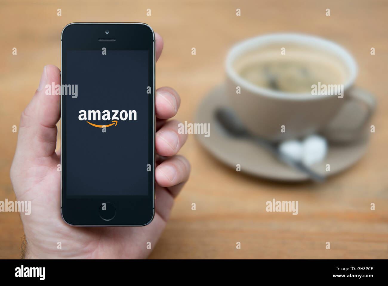 Ein Mann schaut auf seinem iPhone die das Amazon-Logo anzeigt, während bei einer Tasse Kaffee (nur zur redaktionellen Verwendung) saß. Stockfoto