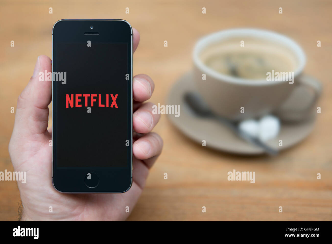 Ein Mann schaut auf seinem iPhone die Netflix-Logo anzeigt, während bei einer Tasse Kaffee (nur zur redaktionellen Verwendung) saß. Stockfoto