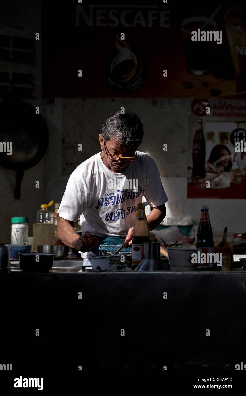 Chefkoch, der im Schatten in einem Gasse Café kocht. Thailand S. E. Asien Stockfoto