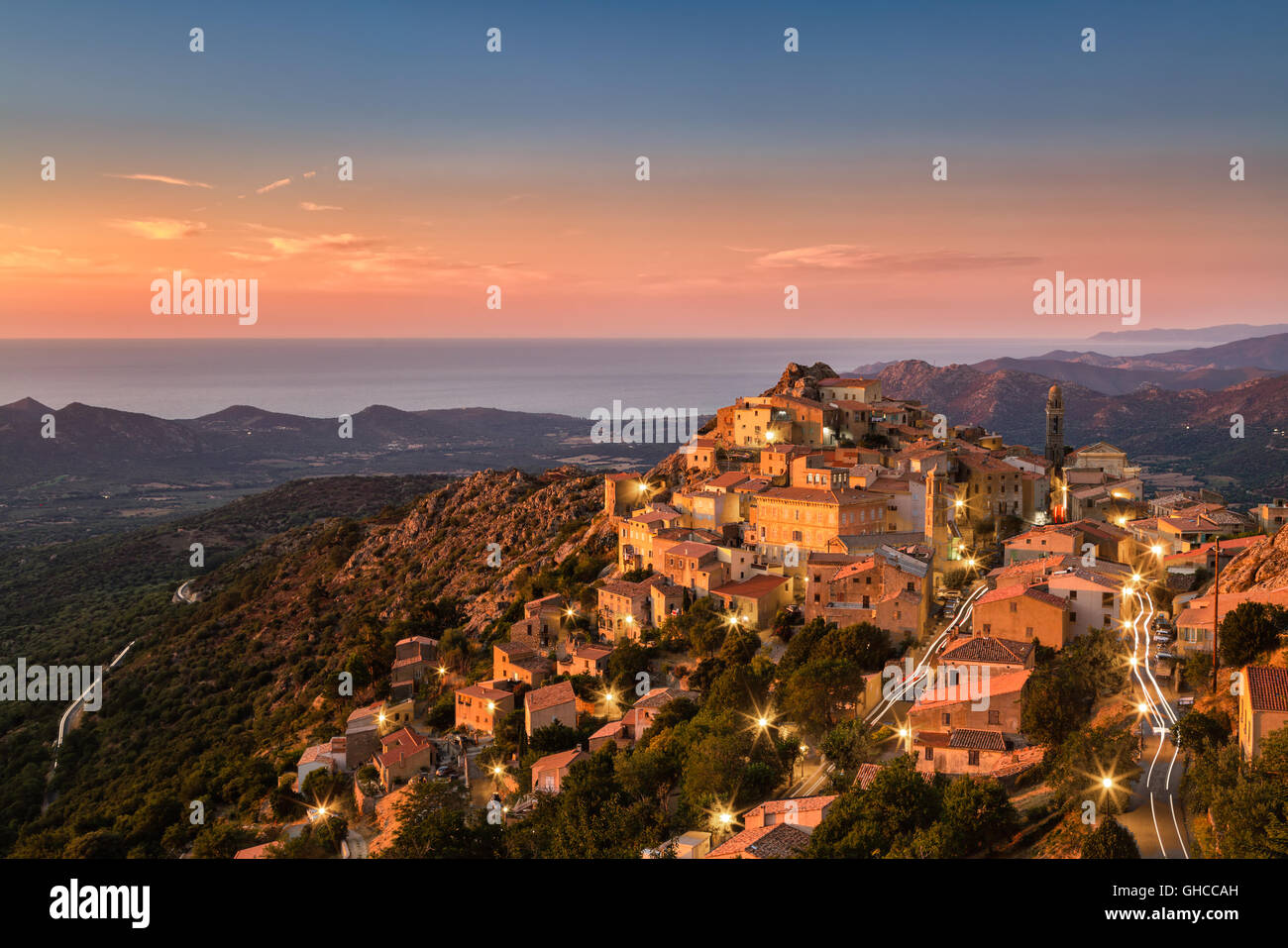 Die Balagne Dorf von Speloncato in Korsika gebadet in den späten Abend Sonnenschein mit Straßenlaternen und Auto Lichtspuren Stockfoto