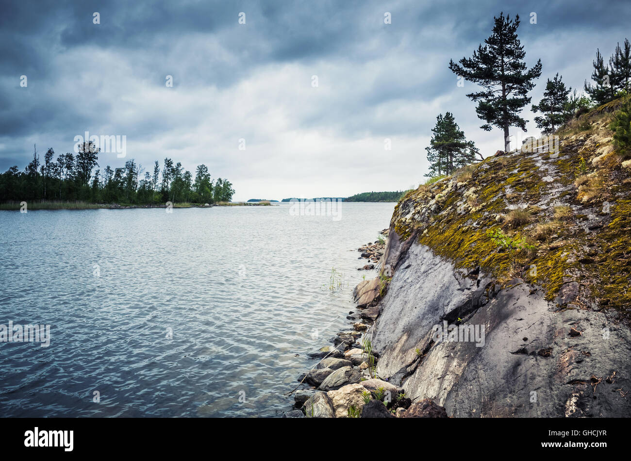Ladoga Seenlandschaft. Kiefern wachsen auf Küstenfelsen unter dunklen dramatischen Wolkenhimmel. Tonwertkorrektur-Foto-Filter-Effekt Stockfoto