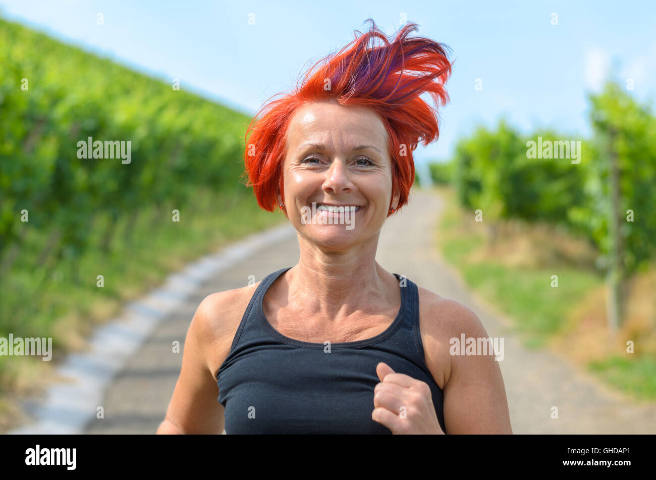 Lächelnde glücklich Frau Joggen in einem Weinberg, die entlang der Landstraße, Nahaufnahme von ihrem Gesicht und fliegenden roten Haare in ein gesundes Leben Stockfoto