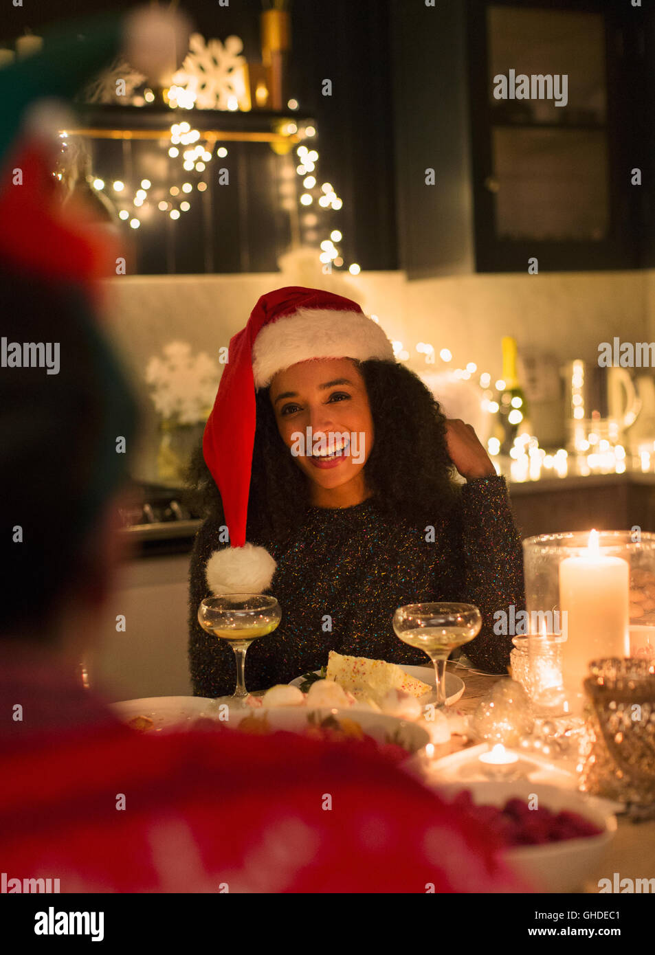 Lächelnde Frau mit Nikolausmütze bei Kerzenlicht Weihnachtsessen Stockfoto