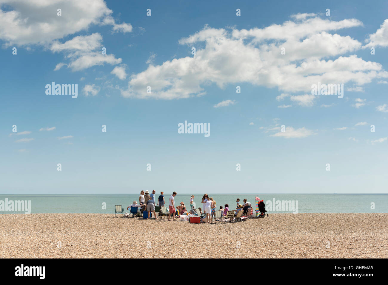 Eine Familie und große Gruppe von Menschen versammeln sich auf dem Kiesstrand in Aldeburgh Suffolk UK im Sommer an einem sonnigen Tag Stockfoto