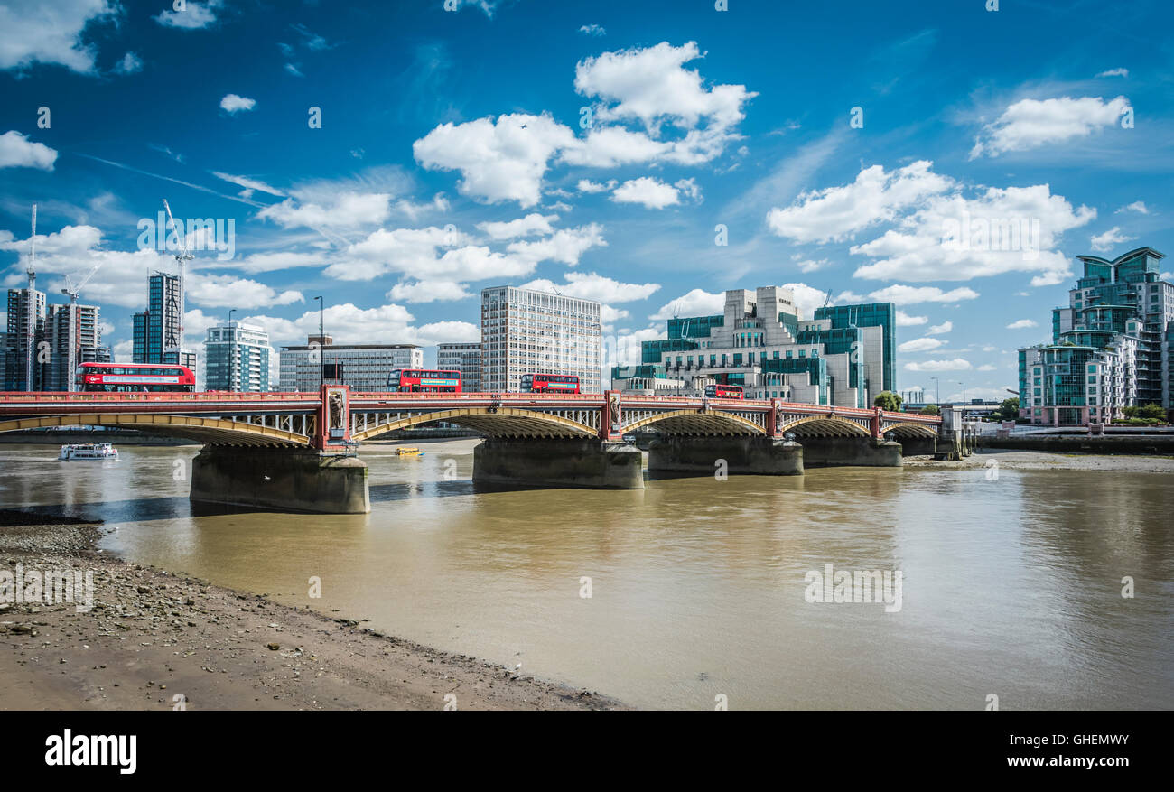 MI6 Hauptquartier (Vauxhall Cross) am Ufer einer schlammigen Themse mit roten TFL Routemaster Bussen, die über die Vauxhall Bridge, London, fahren Stockfoto