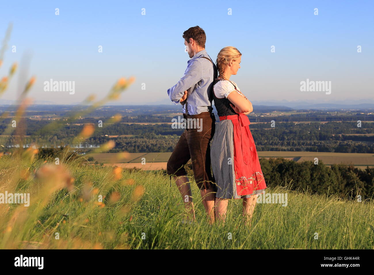 Ein deutsches Paar in bayerischer Tracht Rücken an Rücken auf dem Rasen Stockfoto