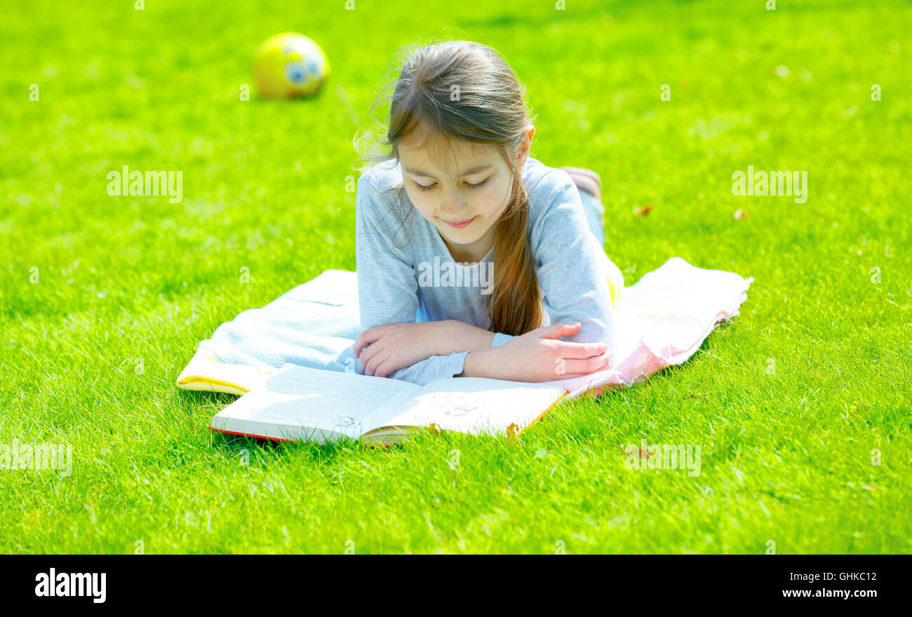 Mädchen lesen Buch auf dem grünen Rasen Stockfoto
