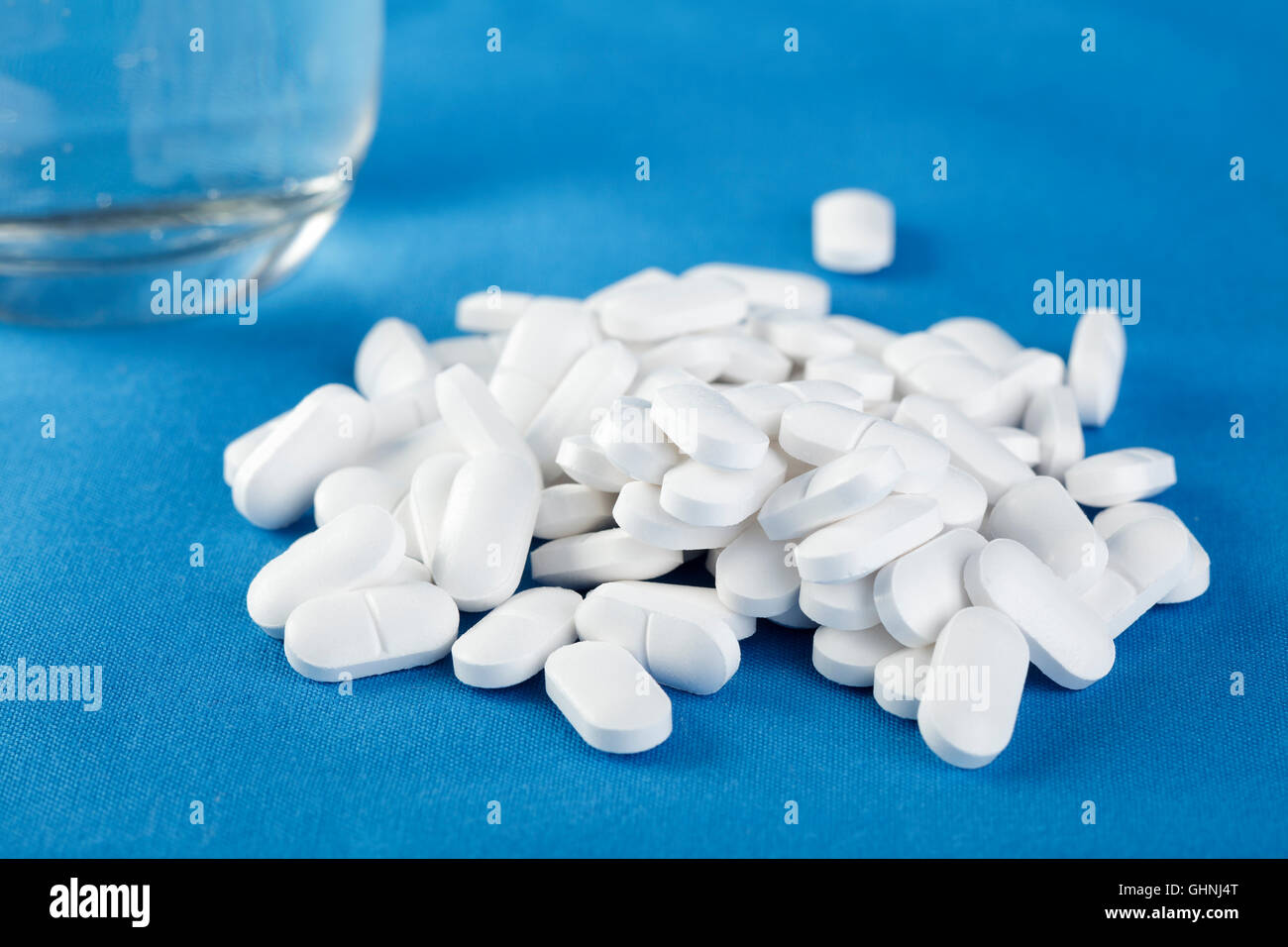 weiße Tabletten und ein Glas Wasser auf einem blauen Hintergrund Stockfoto