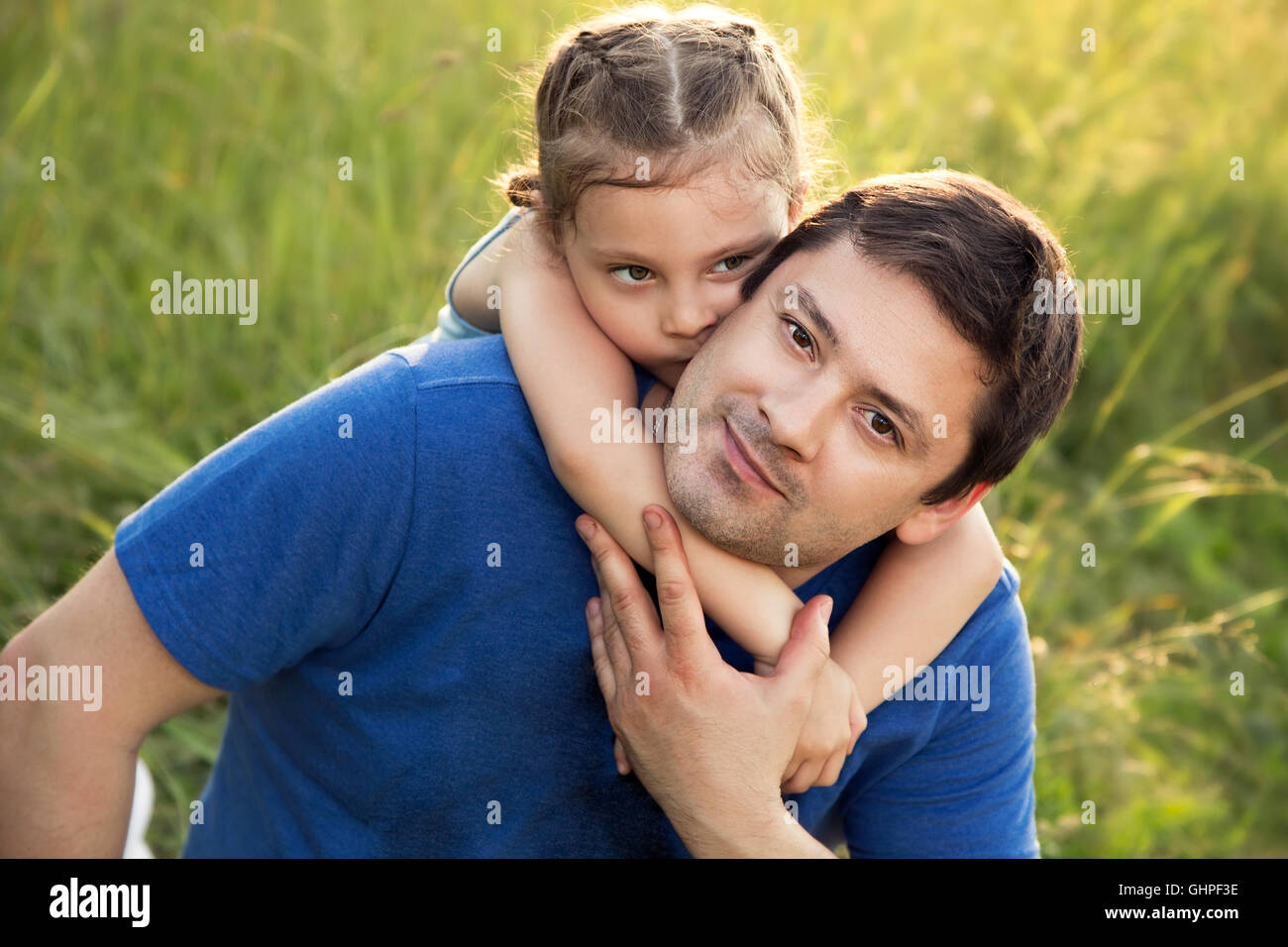 Glückliches Kind Mädchen umarmt mit lieben Vater lächelnd auf Sommer Grasgrün Hintergrund. Closeup portrait Stockfoto