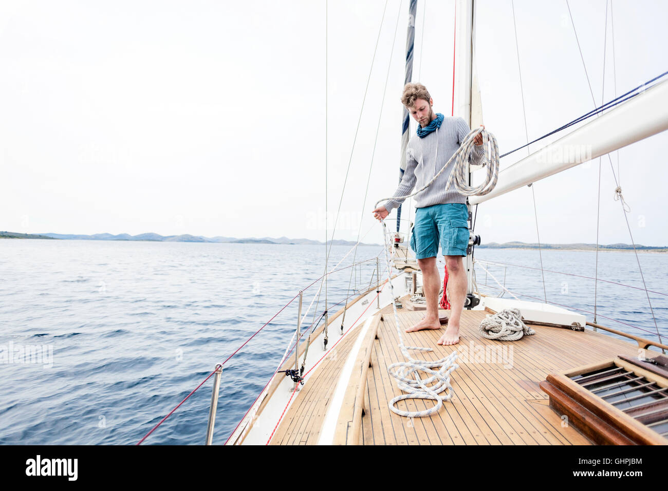 Junger Mann auf Yacht Eisstockschießen Seil Stockfoto