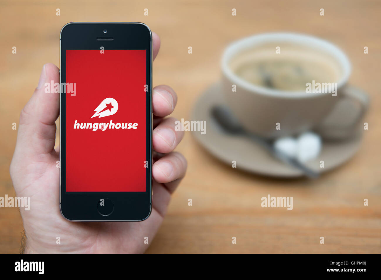 Ein Mann schaut auf seinem iPhone die die hungrigen House-Logo anzeigt, während mit einer Tasse Kaffee (nur zur redaktionellen Verwendung) saß. Stockfoto