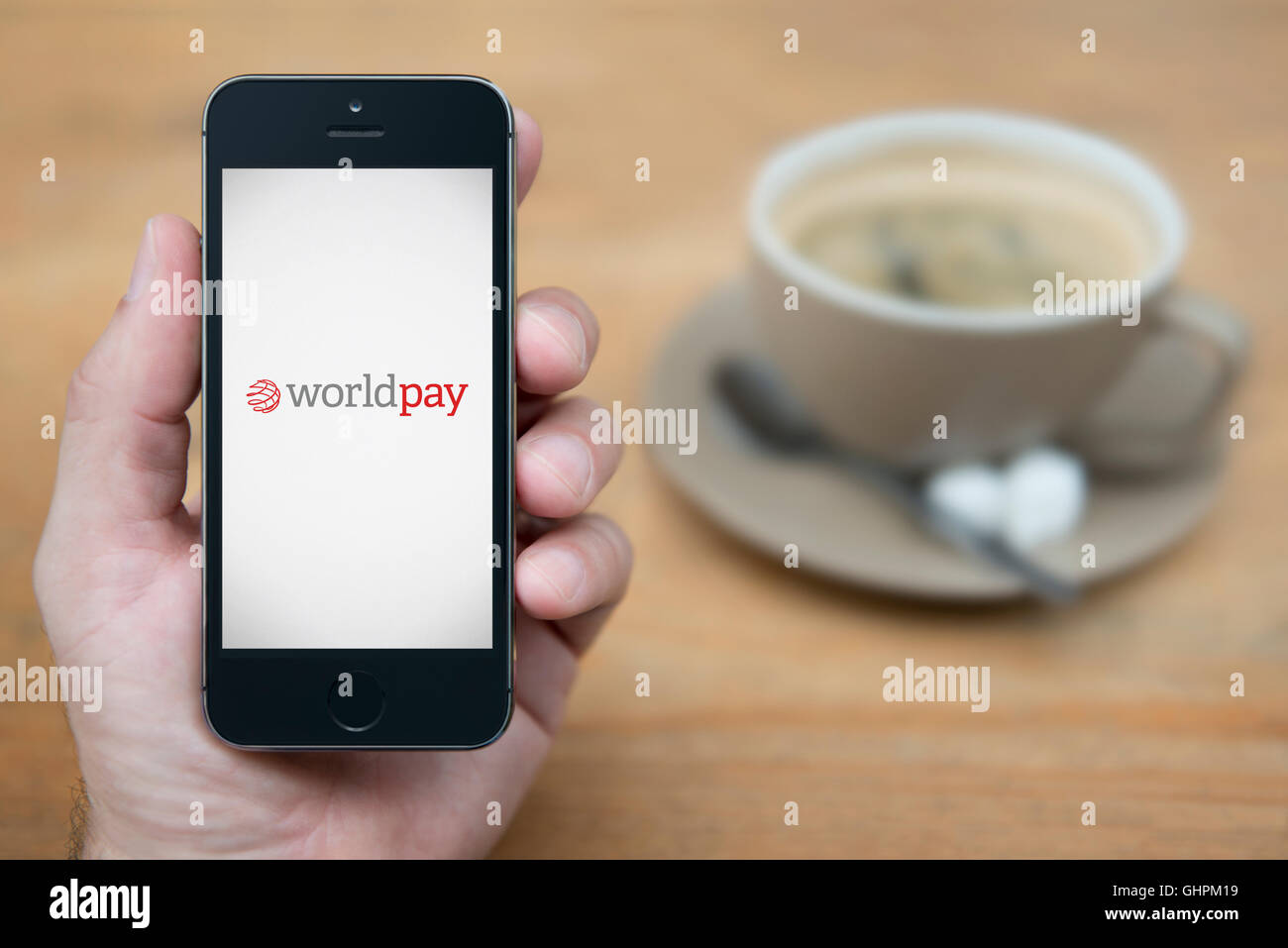 Ein Mann schaut auf seinem iPhone die World Pay-Logo anzeigt, während bei einer Tasse Kaffee (nur zur redaktionellen Verwendung) saß. Stockfoto