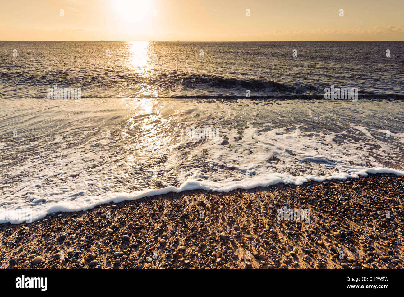 Ein Blick auf das Meer mit sanften Wellen am Strand mit einem niedrigen frühen n Sonne am Morgen im Sommer an einem sonnigen Tag Stockfoto