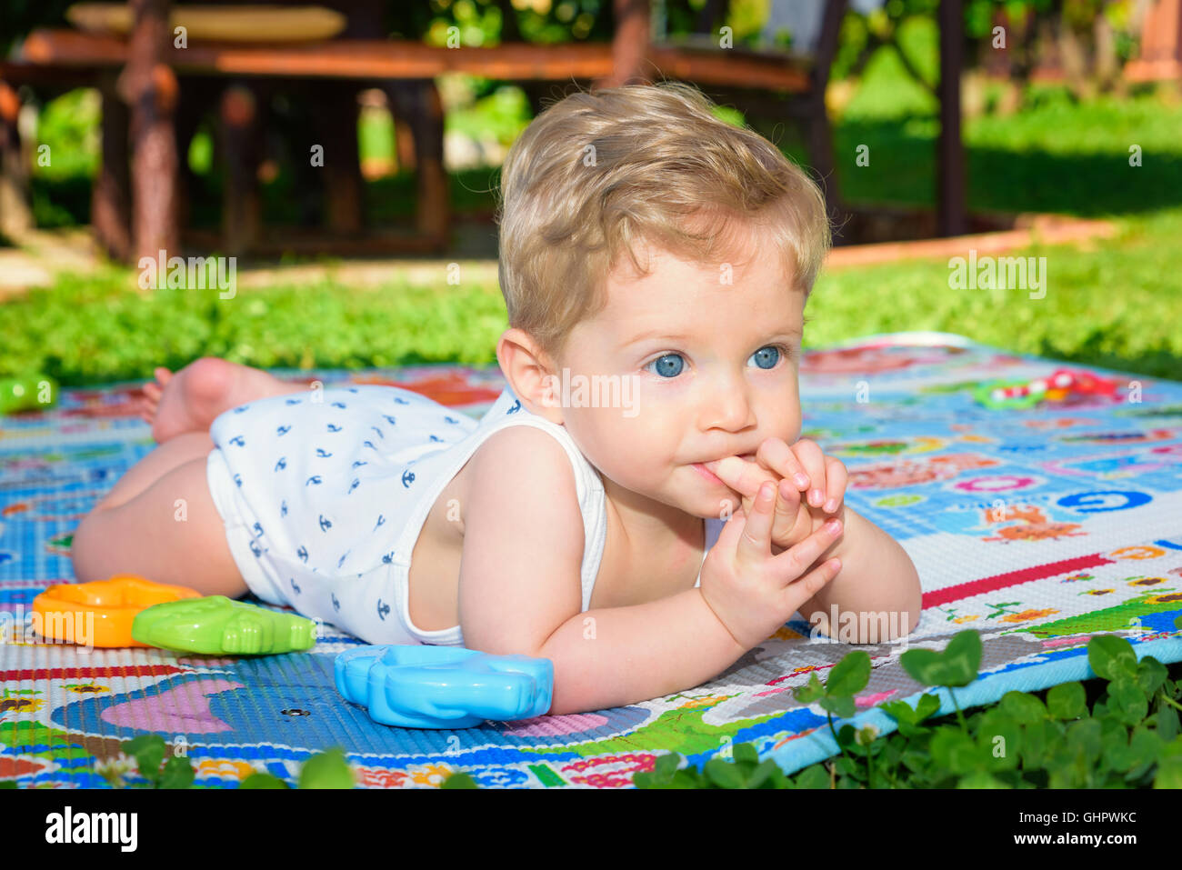 Acht Monate alten schönen Baby Boy mit Finger im Mund, im Garten krabbeln hautnah. Stockfoto