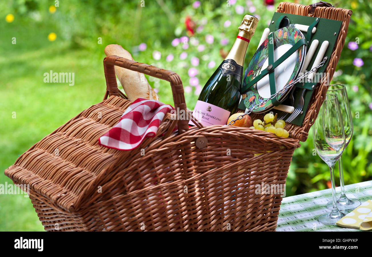 Englischer Sparkling Rosé Weinflasche und Weidenkorb Picknickkorb Korb Korb Baguette Trauben Obst in sonniger floraler UK Garten Situation Stockfoto