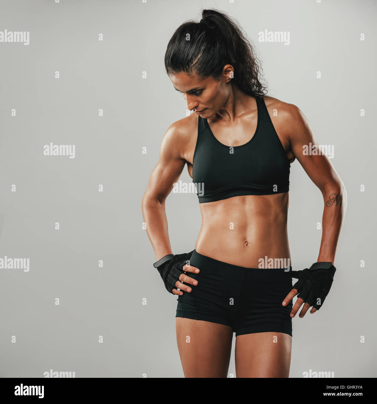 Muskuläre sportliche junge Frau in Sportkleidung posiert mit ihr die Hände auf ihre Hüften nach unten, quadratisches Format auf grau Stockfoto