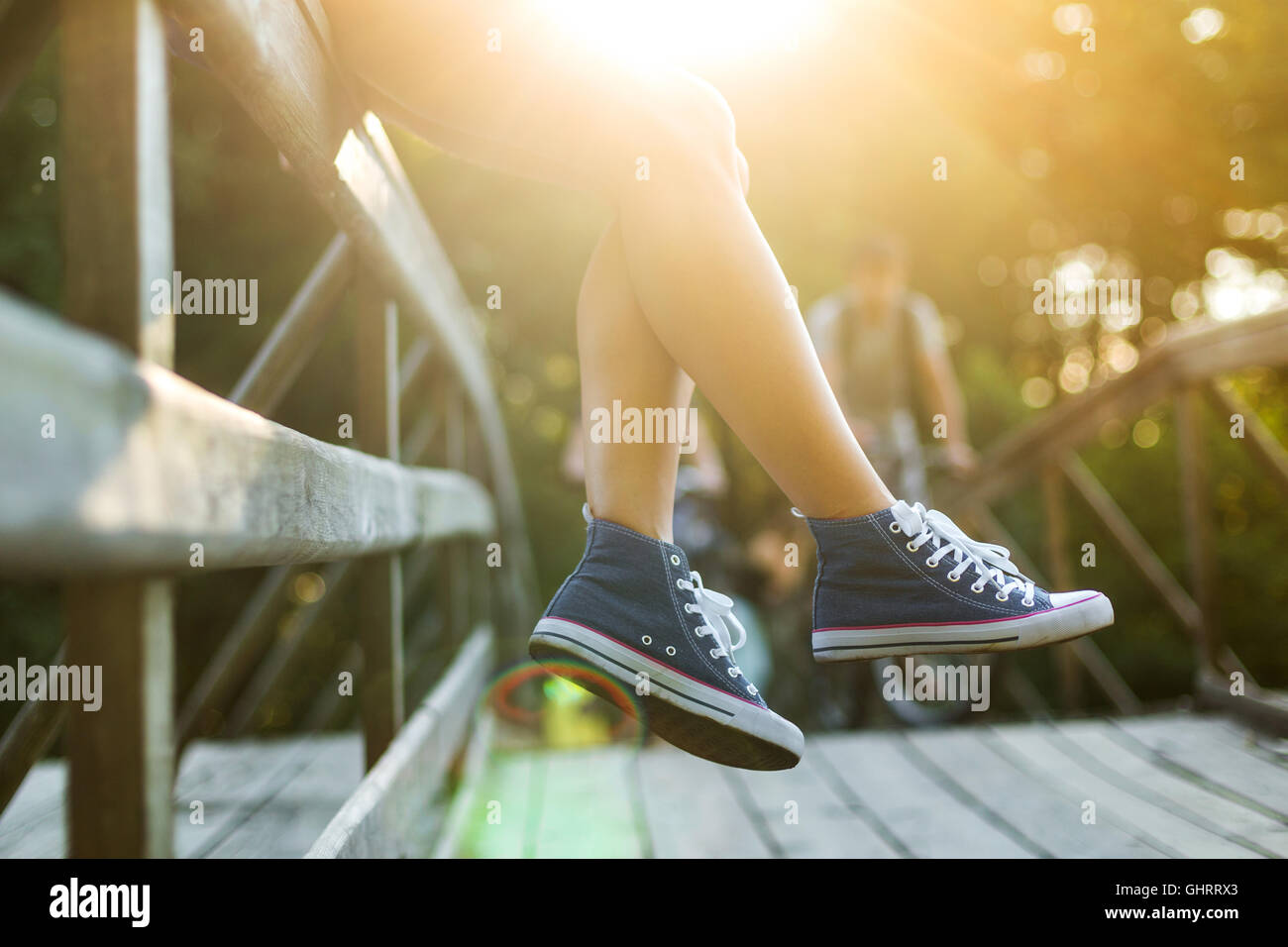 Junge Frau mit schönen sportlichen Beinen sitzen auf einer Holzbrücke Geländer in Jeans Turnschuhen Stockfoto