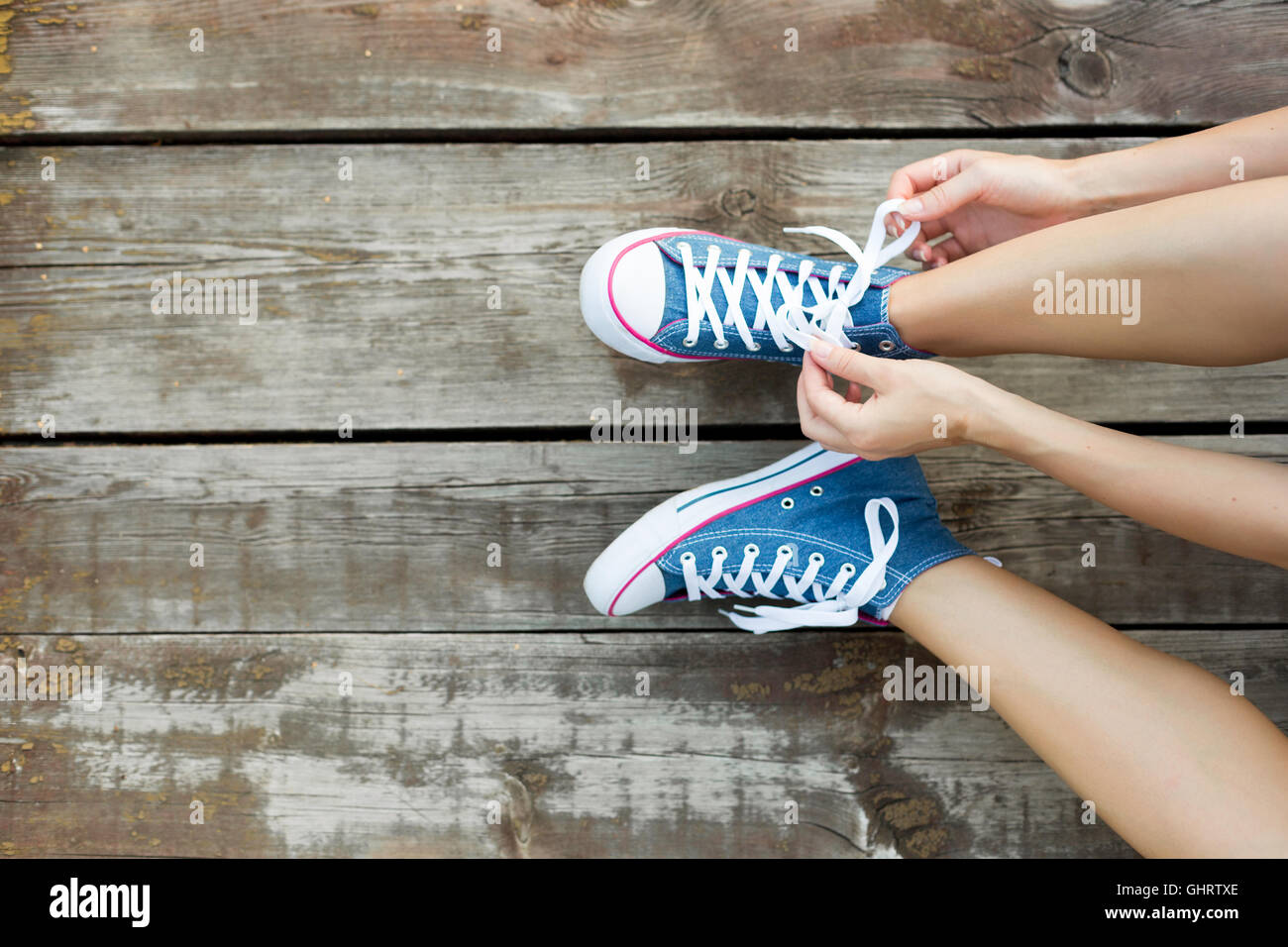 Junge Frau binden Schnürsenkel ihrer Jeans Sneaker sitzt auf dem Holzboden Stockfoto