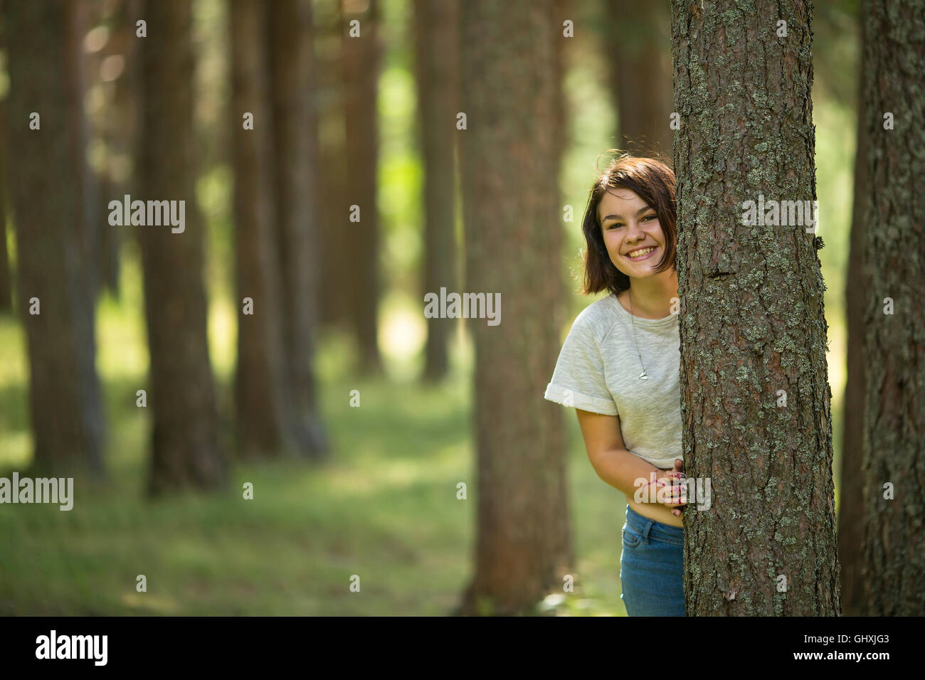 Ein junges Mädchen steht an einem Baum im Park und lächelt. Stockfoto
