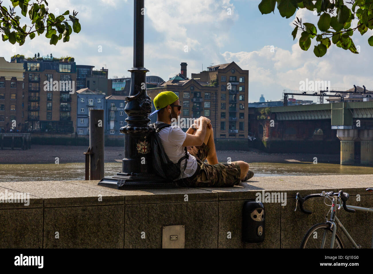 Mann sitzt auf einer Mauer an der Themse in der Nähe von Cannon Street Railway Bridge, London, England, Vereinigtes Königreich Stockfoto