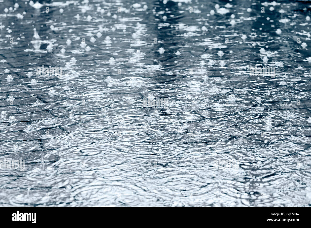 überflutete Kopfsteinpflaster mit Pfützen von Wasser und Regentropfen Stockfoto