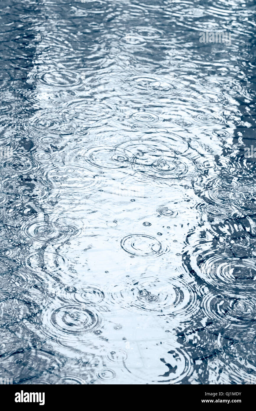 Gehweg mit Pfützen von Wasser und Regentropfen bei starkem Regen Stockfoto