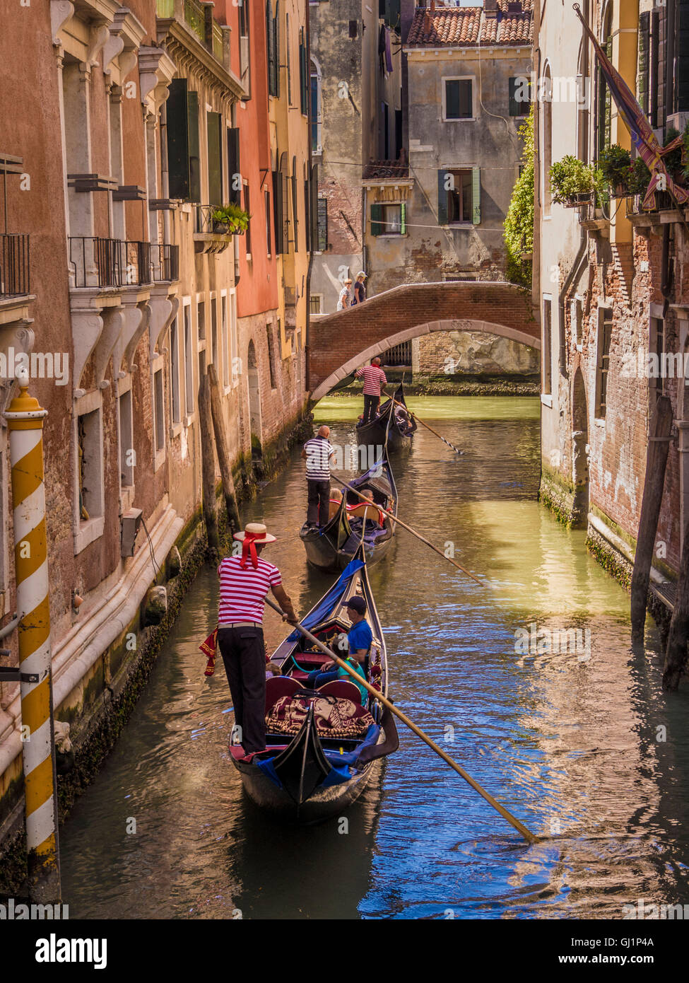 Gondoliere tragen traditionelle gestreiften Oberteil und Strohhut Hut Lenkung seine Gondel an einem Kanal hinter 2 andere Gondeln. Venedig Stockfoto