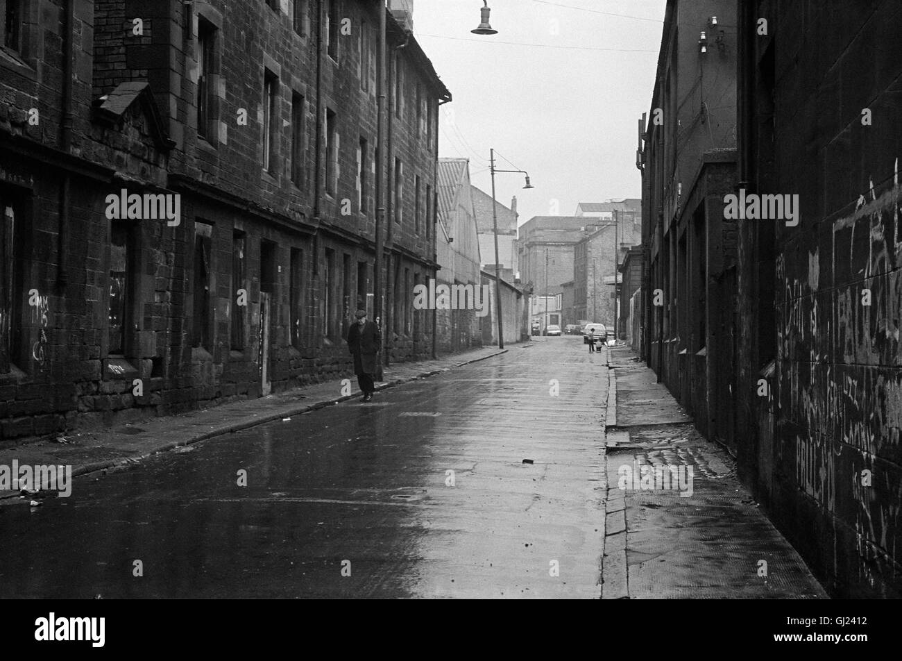 Mann zu Fuß entlang der nassen Straße in Calton Gegend von Glasgow East End, 1971 ca. Stockfoto