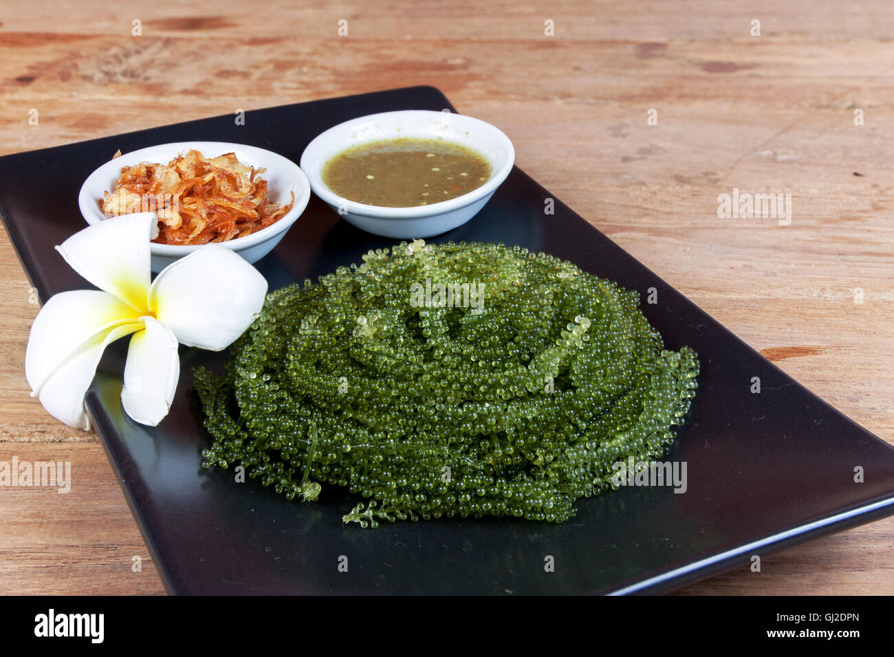 Meer Trauben oder grünen Kaviar und pikanter Sauce auf einem schwarzen Schale der Holztisch Stockfoto