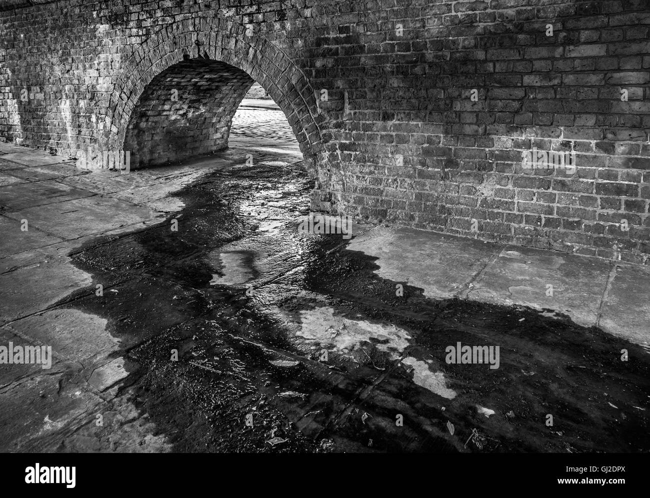 Alte viktorianischen Backstein Bogen in städtischen Straße mit fließendem Wasser. Stockfoto