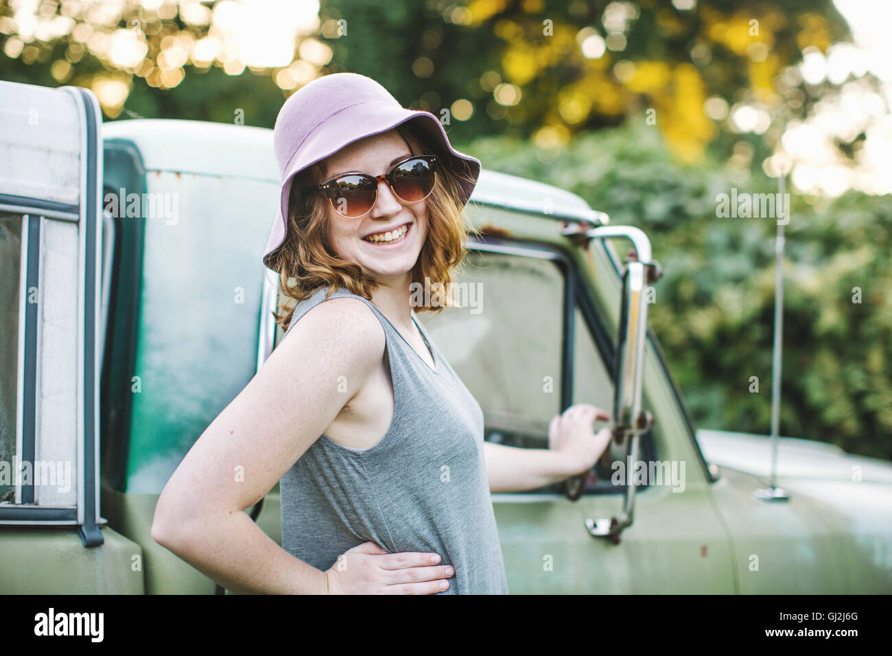 Frau mit Sonnenhut und eine Sonnenbrille, die auf der Suche über die Schulter in die Kamera Lächeln Stockfoto