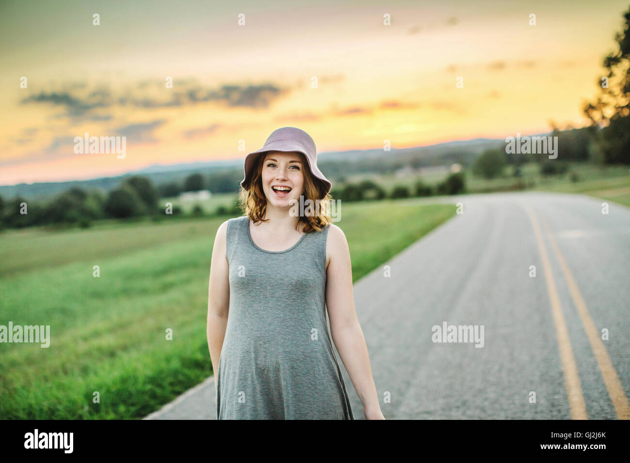 Frau auf Landstraße tragen Sonnenhut Blick auf die Kamera zu Lächeln Stockfoto