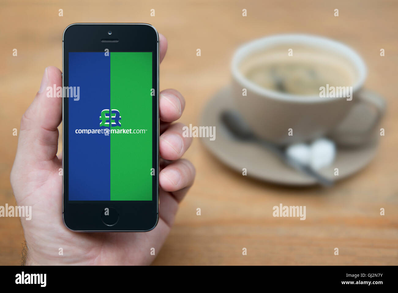 Ein Mann schaut auf seinem iPhone, zeigt die dem Markt Logo vergleichen, während Sie sitzen mit einer Tasse Kaffee (nur redaktionelle Nutzung). Stockfoto