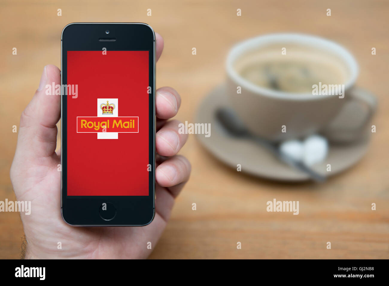 Ein Mann schaut auf seinem iPhone die Royal Mail-Logo anzeigt, während bei einer Tasse Kaffee (nur zur redaktionellen Verwendung) saß. Stockfoto