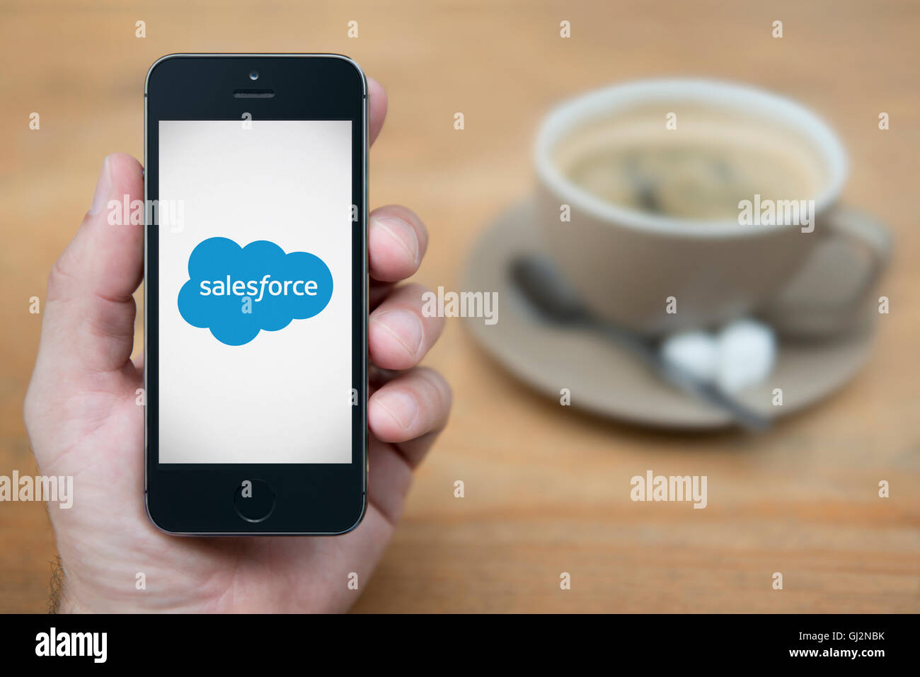 Ein Mann schaut auf seinem iPhone die SalesForce-Logo anzeigt, während bei einer Tasse Kaffee (nur zur redaktionellen Verwendung) saß. Stockfoto