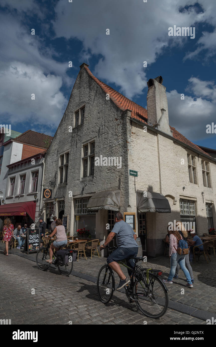 Touristen und einheimische Wandern und Radfahren in der Sonne entlang der gepflasterten Straßen von Brügge. Stockfoto