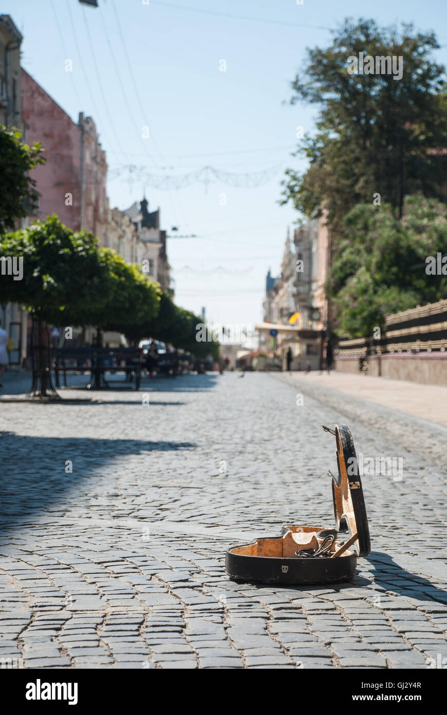 Pflaster auf der Straße der Altstadt. Der Hintergrund jedoch unscharf. Im Vordergrund ist ein offener Fall vom Violoncello. Stockfoto