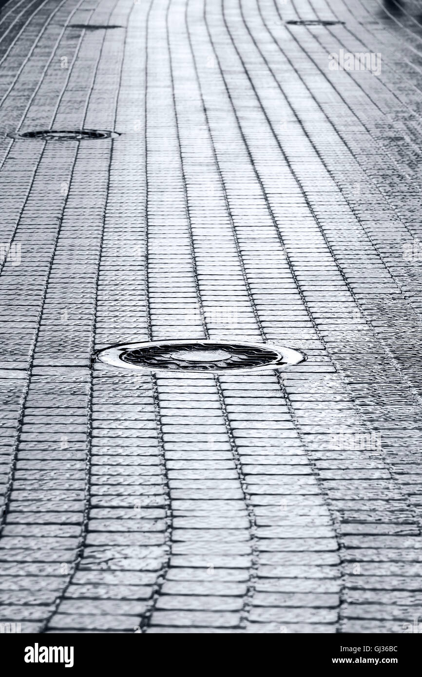 Metall Kanalisation Kanaldeckel auf dunklen nassen Kopfsteinpflaster Stockfoto