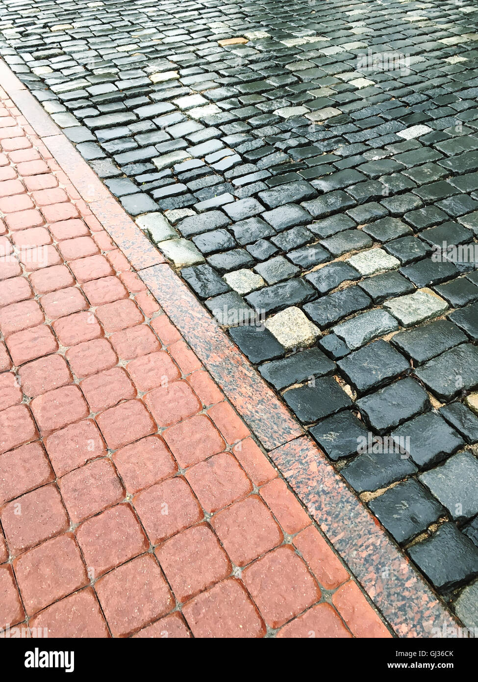 Feuchte alte Granit gepflasterten Straße mit farbigen Zement Ziegel Bürgersteig Stockfoto