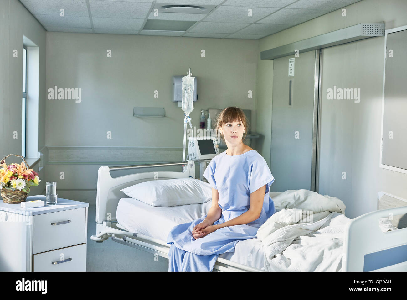 Patient sitzt am Krankenhaus Bett tragen Krankenhemd Stockfoto