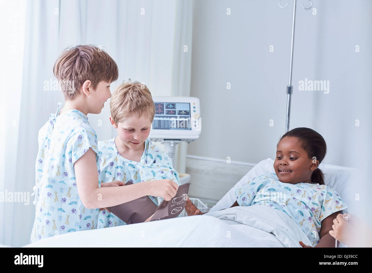 Junge Patienten mit Blutdruckmanschette auf Freund im Bett im Krankenhaus Kinderstation Stockfoto