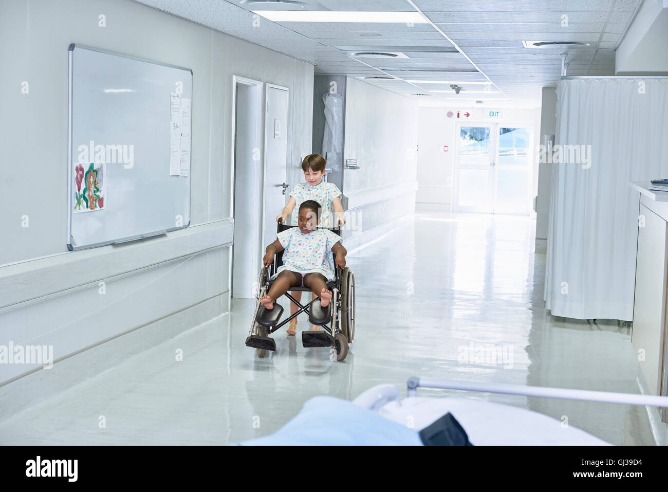 Junge Patienten drängen Freundin im Rollstuhl am Krankenhaus Kinderstation Stockfoto