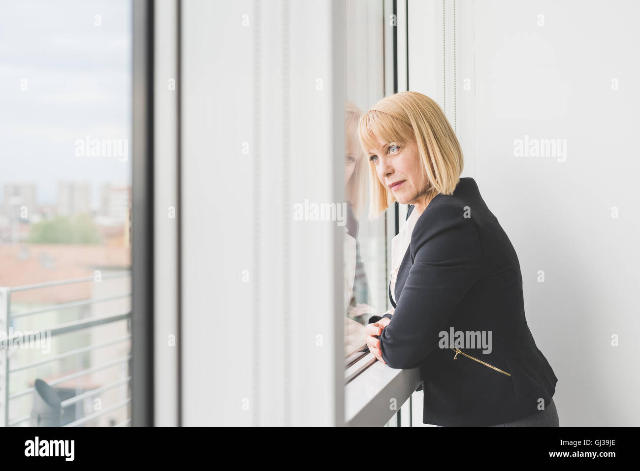 Reife Geschäftsfrau gelehnt und starrte durch Bürofenster Stockfoto