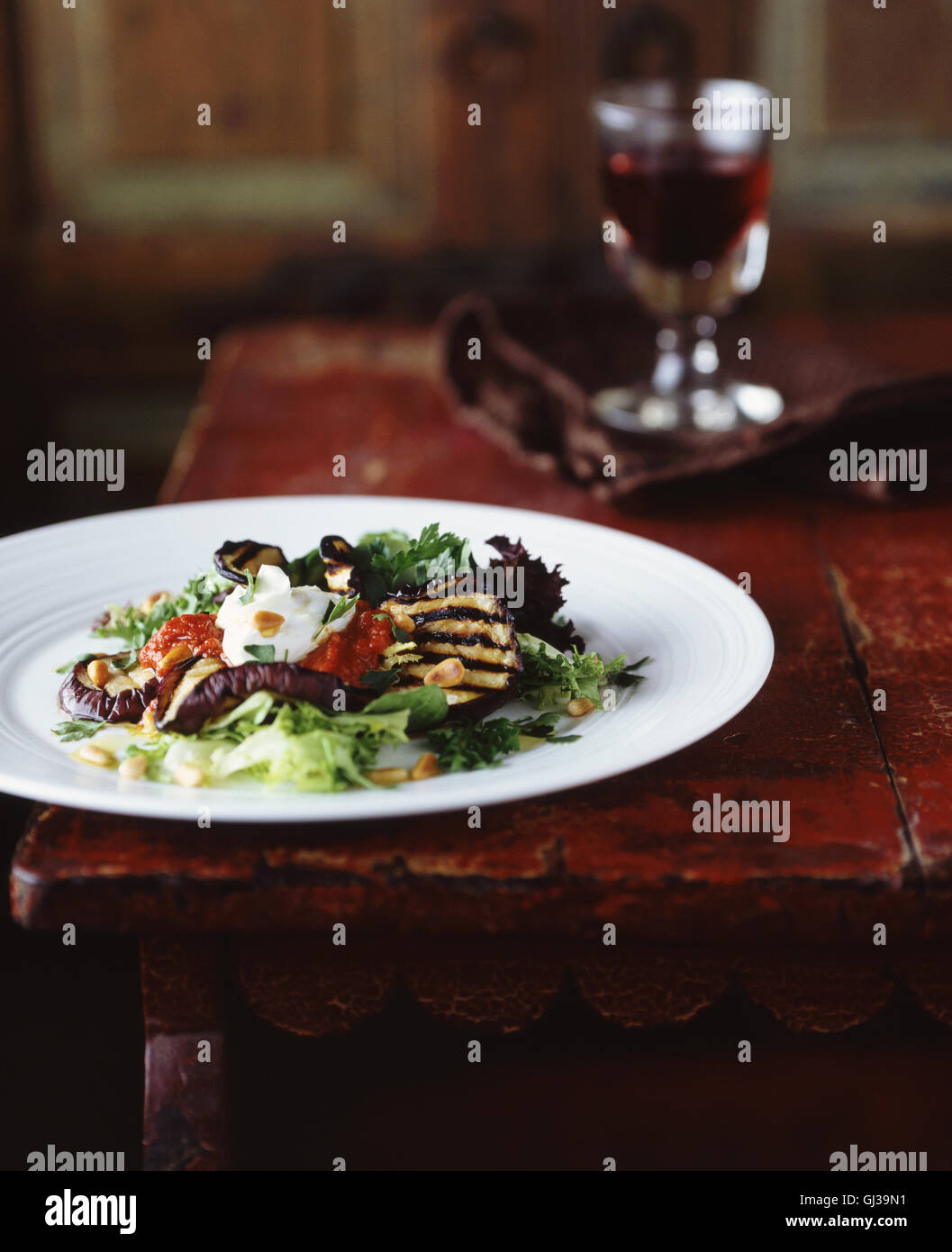 Gegrillte Auberginen und Pinienkernen Salat mit Glas Rotwein Stockfoto