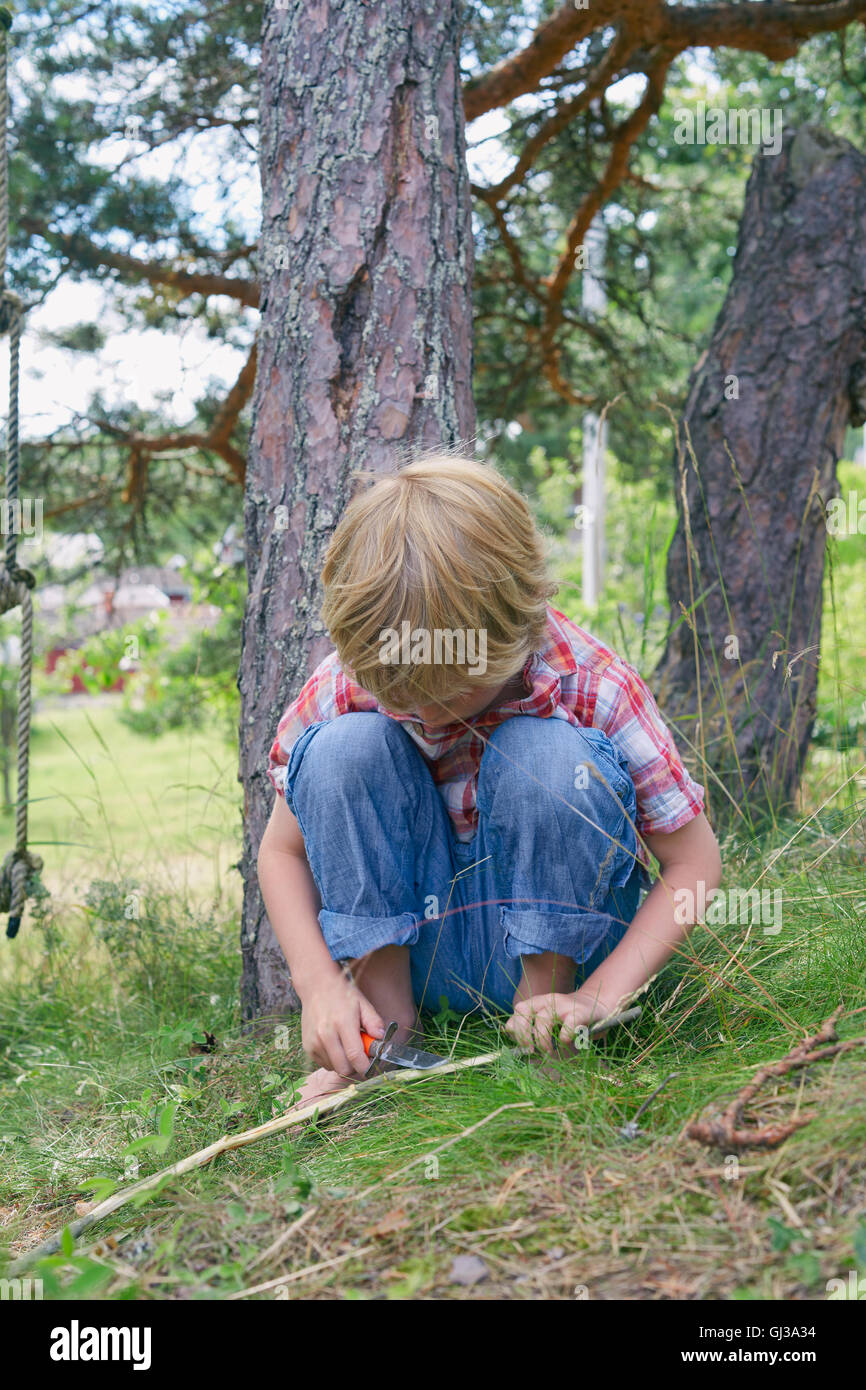 Kleiner Junge Reinigung Ast mit Messer Stockfoto