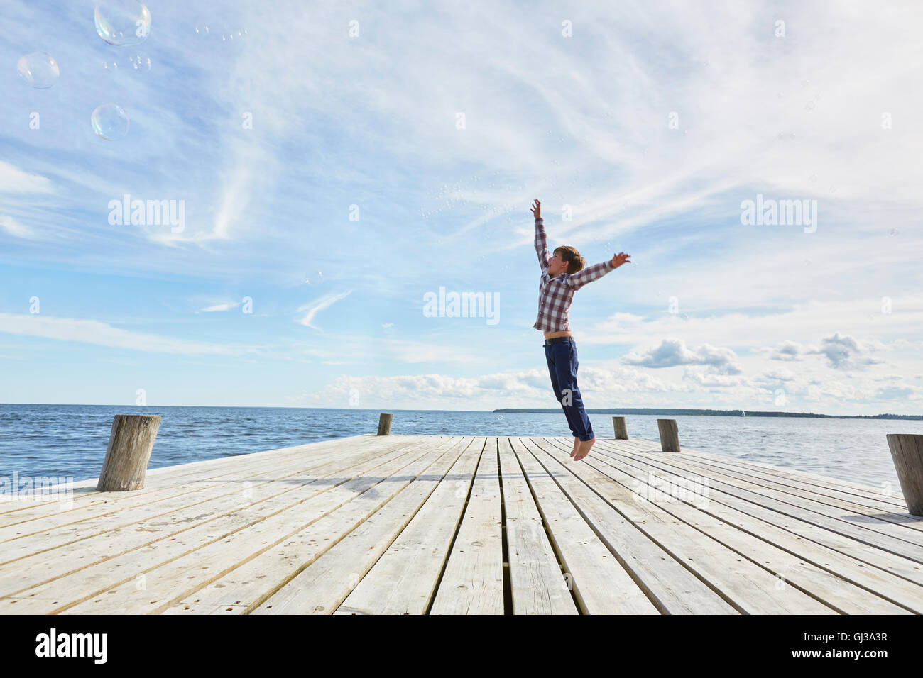 Junge auf Holzsteg, springen, um Luftblasen zu erreichen Stockfoto