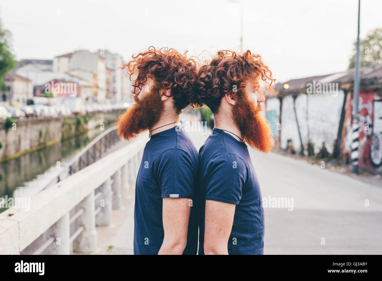 Porträt des jungen männlichen Hipster Zwillinge mit dem roten Haar und Bärte Rücken an Rücken auf Brücke Stockfoto